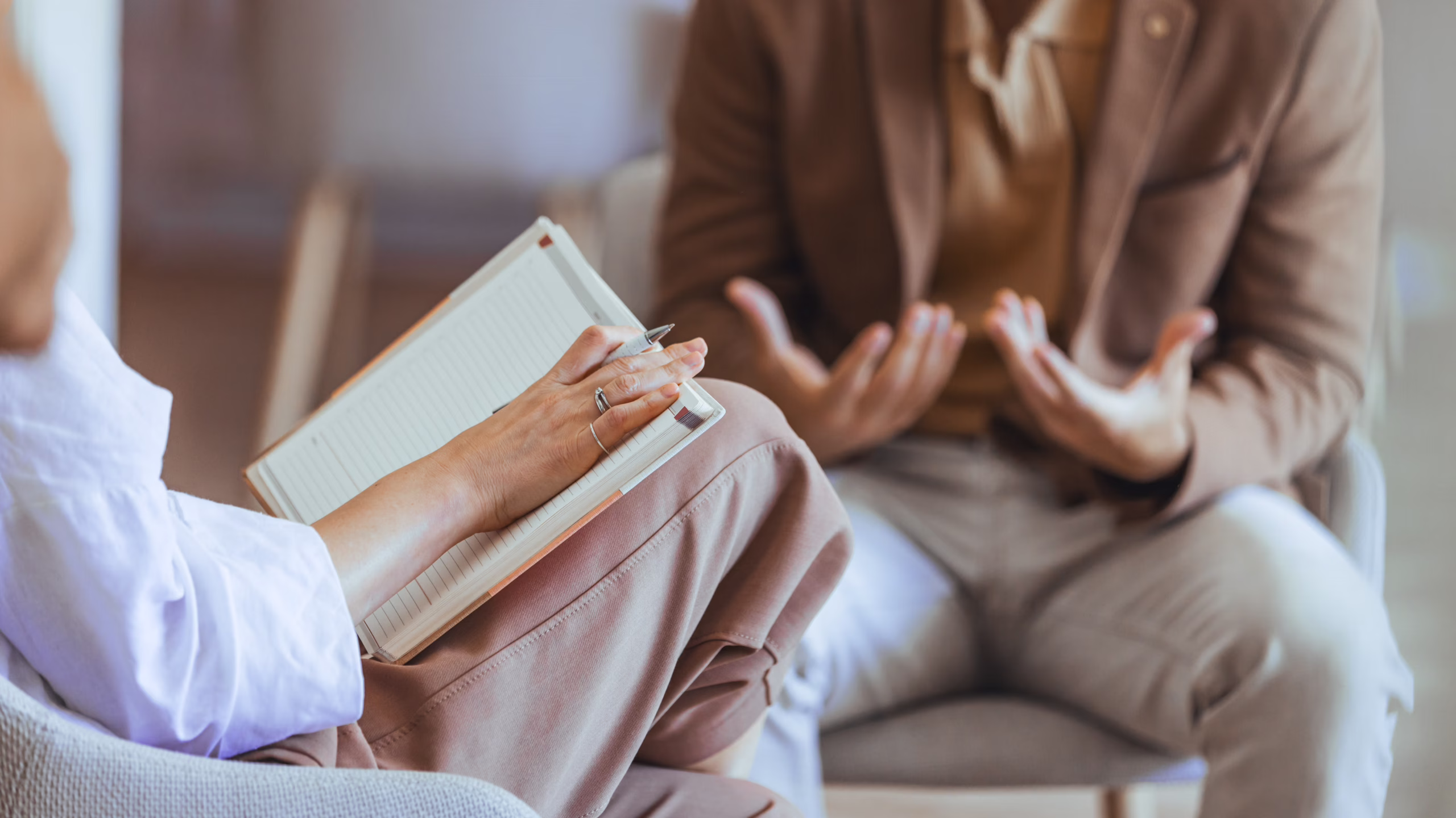 A coach takes notes in a journal while listening intently to a tenant who is gesturing as they speak during Coaching Plus support session.